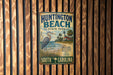 A vintage metal sign for Huntington Beach State Park in South Carolina, featuring a heron and a lighthouse, is displayed on a wooden wall.