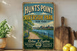 A vintage-style metal sign for "HUNTS POINT RIVERSIDE A PARK NEW YORK" is displayed on a shelf, with a potted plant and a wooden cutting board nearby.