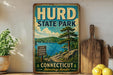 A vintage-style sign for Hurd State Park in Connecticut, featuring a scenic landscape with a lake, mountains, and pine trees.