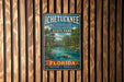 A vintage-style metal sign for Ichetucknee Springs State Park in Florida, featuring a scenic illustration of the springs surrounded by lush greenery and a manatee.