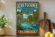 A vintage-style sign for Ichetucknee Springs State Park in Florida, featuring a scenic illustration of a manatee in a river surrounded by palm trees.
