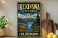 A vintage-style sign for Ike Kinswa State Park in Washington, featuring a mountain landscape and a river, with the text "Adventure Awaits" and "Washington" below.
