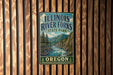 A vintage metal sign for Illinois River Falls State Park in Oregon, featuring a scenic landscape with a river, mountains, and pine trees.
