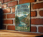 A vintage-style metal sign for Illinois River Forks State Park, featuring a scenic image of the river surrounded by mountains and forests.