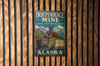 A vintage-style sign for Independence Mine, a state historical park in Alaska, featuring a train and mountains in the background.
