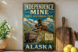 A vintage-style sign for Independence Mine, a state historical park in Alaska, featuring a train and a mountain landscape.