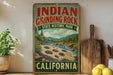 A vintage-style sign for Indian Grinding Rock State Historic Park in California, featuring a scenic landscape with mountains, a river, and a grinding stone.