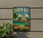 A vintage-style sign for Indian Key Historic State Park in Florida, featuring a tropical beach scene with palm trees and a small building.