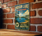 A vintage metal sign advertising Indian Lake State Park in Ohio, featuring a scenic illustration of a lake surrounded by trees and a sailboat.