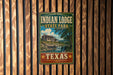 A vintage-style metal sign for Indian Lodge State Park in Texas, featuring a scenic illustration of a cabin and waterfall.