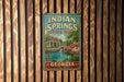A vintage metal sign for Indian Springs State Park in Georgia, featuring a scenic illustration of a pond, waterfall, and surrounding landscape.
