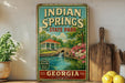 A vintage-style sign for Indian Springs State Park in Georgia, featuring a scenic illustration of a gazebo and a pond surrounded by lush greenery.