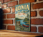 A vintage-style metal sign for the Ionia State Recreation Area in Michigan, featuring a scenic illustration of a lake, forest, and canoe.