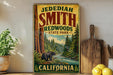 A vintage-style sign for Jedediaah Smith Redwoods State Park in California, featuring a scenic illustration of a bear in the foreground and a river in the background.