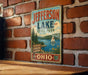 A vintage-style metal sign for Jefferson Lake State Park in Ohio, featuring a scenic illustration of the lake and surrounding landscape.