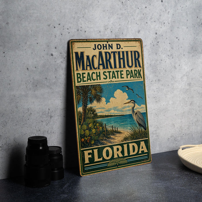 A vintage-style sign for John D. Mac Arthur Beach State Park in Florida, featuring a beach scene with palm trees and a bird.