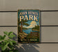 A vintage-style sign for John Henes Park in Wisconsin, featuring a scenic landscape with a lake and pine trees.