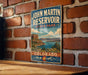 A vintage-style sign for John Martin Reservoir, a state park in Colorado, is displayed on a brick wall.