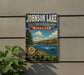 A vintage-style metal sign for Johnson Lake, Nebraska, featuring a scenic image of a lake surrounded by mountains and a boat on the water.