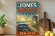 A vintage-style sign for Jones Beach State Park in New York, featuring a beach scene with a lighthouse and a welcome sign.