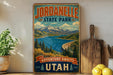 A vintage-style sign for Jordanelle State Park, featuring a scenic mountain landscape with a lake and pine trees.