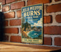 A vintage-style metal sign for Julia Pfeiffer Burns State Park in California, featuring a scenic coastal landscape with a beach, mountains, and a body of water.