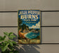 A vintage-style metal sign for Julia burns State Park in California, featuring a scenic coastal landscape with palm trees, a waterfall, and a beach.