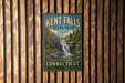A vintage metal sign for Kent Falls State Park in Connecticut, featuring a waterfall surrounded by trees and a forested landscape.