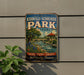 A vintage metal sign for Kerrville-Schreiner Park in Texas, featuring a scenic illustration of a river, bridge, and surrounding landscape.