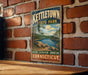 A vintage metal sign for kettletown state park hangs on a brick wall, featuring a scenic landscape with a lake and mountains.