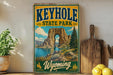 A vintage-style sign for Keyhole State Park in Wyoming, featuring a scenic landscape with a large rock formation, a lake, and mountains in the background.