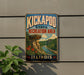 A vintage-style sign for the Kickapoo State Recreation Area in Illinois, featuring a scenic landscape with a river, cliffs, and flowers.