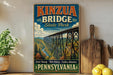 A vintage-style poster of Kinzua Bridge in Pennsylvania, featuring a scenic view of the bridge and surrounding landscape.
