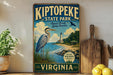 A vintage-style sign for Kiptopek State Park, featuring an illustration of a heron and a lighthouse, with the text "Kiptopek State Park" and "Natural Beauty Lasting Memories" prominently displayed.