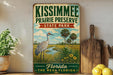 A vintage-style sign for Kissimmee Prairie Preserve, featuring a bird and palm trees, is displayed on a shelf next to a wooden cutting board and some lemons.