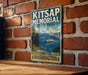 A vintage-style metal sign for Kitsap Memorial State Park in Washington, featuring a scenic image of a mountain, water, and a ferry boat.