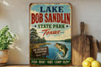 A vintage-style sign for Lake Bob Sandlin State Park in Texas, featuring a fishing scene and a sign that says "An Outdoor Tradition Since 1977".