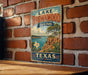 A vintage-style metal sign for Lake Brownwood State Park in Texas, featuring a scenic illustration of the park's landscape.