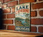 A vintage-style sign for Lake Catherine State Park in Arkansas, featuring a scenic landscape with a lake, mountains, and a sign indicating the park's name.