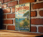 A vintage metal sign for LakeCorpus Christi State Park in Texas, featuring a scenic illustration of the lake and surrounding landscape.