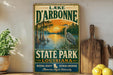 A vintage-style sign for Lake D'Arbonne State Park in Louisiana, featuring a scenic illustration of a lake, palm trees, and a bird.