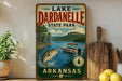 A vintage-style sign for Lakeardelle State Park in Arkansas, featuring a scenic illustration of a lake, mountains, and a boat.