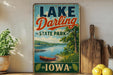 A vintage-style sign for Lake Darling State Park in Iowa, featuring a scenic illustration of a lake, canoe, and surrounding landscape.
