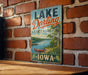 A vintage-style metal sign for Lake Darling State Park in Iowa, featuring a scenic illustration of a lake and surrounding landscape.