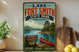 A vintage-style sign for Lake Fort Smith State Park in Arkansas, featuring a scenic illustration of a lake, mountains, and a canoe.