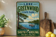 A vintage-style sign for Lake Greenwood State Park in South Carolina, featuring a scenic image of a lake with a boat and trees.