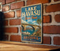 A vintage-style sign for Lake Havasu State Park in Arizona, featuring a scenic illustration of a bridge, boats, and palm trees.