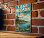 A vintage metal sign for Lake Hudson, the Lake Hudson Recreation Area in Michigan, is displayed on a brick wall.