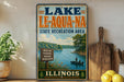 A vintage-style sign for Lake Le-Aqua-NA, a state recreation area in Illinois, featuring a scenic image of a lake with a boat and people fishing.