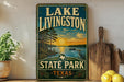 A vintage-style sign for Lake Livingston State Park in Texas, featuring a scenic landscape with a sunset over a lake and a bird in flight.